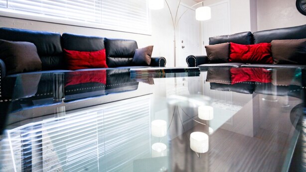 Una sala de estar moderna con una mesa de centro de vidrio, sofás de cuero y cojines rojos y marrones, e iluminación colgante.