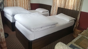 A hotel room with two single beds, a wooden headboard, a wicker side table, and a patterned rug.