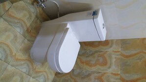A toilet with a bidet attachment, a hand dryer, and a soap dispenser.