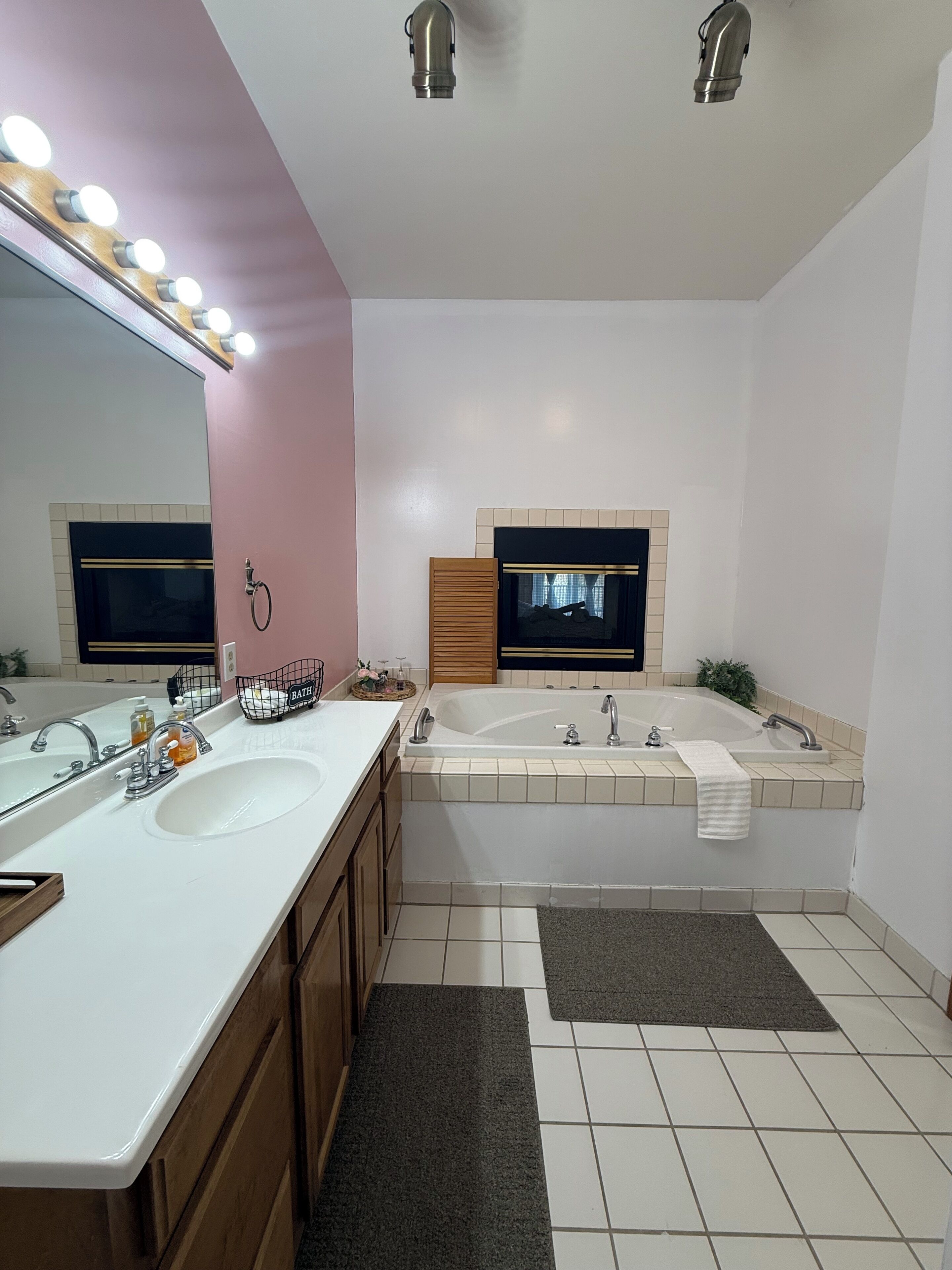 Ein modernes Badezimmer mit zwei Waschbecken, einer Badewanne, einem großen Spiegel mit Beleuchtung und einem Fernseher über der Wanne.