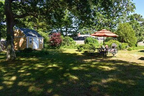Ein Haus mit kleinem Garten, einem Picknicktisch und einem roten Sonnenschirm.