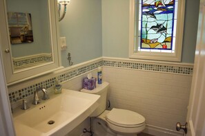 Ein Badezimmer mit einem weißen Waschbecken, einer Toilette und einem Buntglasfenster über der Toilette, das Delfine zeigt.
