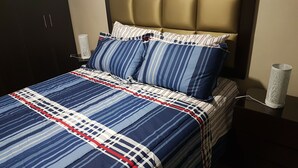 Ein Bett mit einer gesteiften, blau-weiß gestreiften Tagesdecke, zwei Kissen mit Streifenmuster, einem Kopfteil und je einer weißen Lampe auf beiden Seiten.