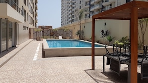 Ein Poolbereich mit gefliestem Boden, einer Pergola und Sitzgelegenheiten im Freien.