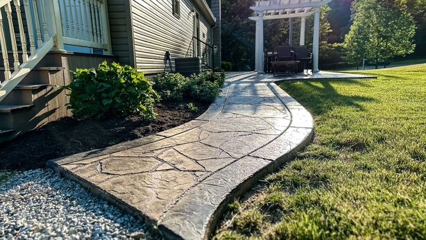 A stone pathway leading to a house with a porch and a pergola.