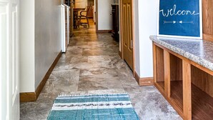 A hallway with a welcome sign, wooden cabinets, and a tiled floor.