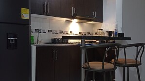 A modern kitchen with dark cabinets, a refrigerator, a gas stove, and two bar stools. - SUPERHOST APARTAMENTO, EXCELENTE UBICACION TULIPAN (Cúcuta)