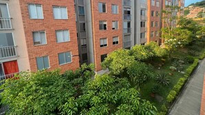 A multi-story residential building with a brick facade, balconies, and a well-maintained garden area with various plants and trees. - SUPERHOST APARTAMENTO, EXCELENTE UBICACION TULIPAN (Cúcuta)