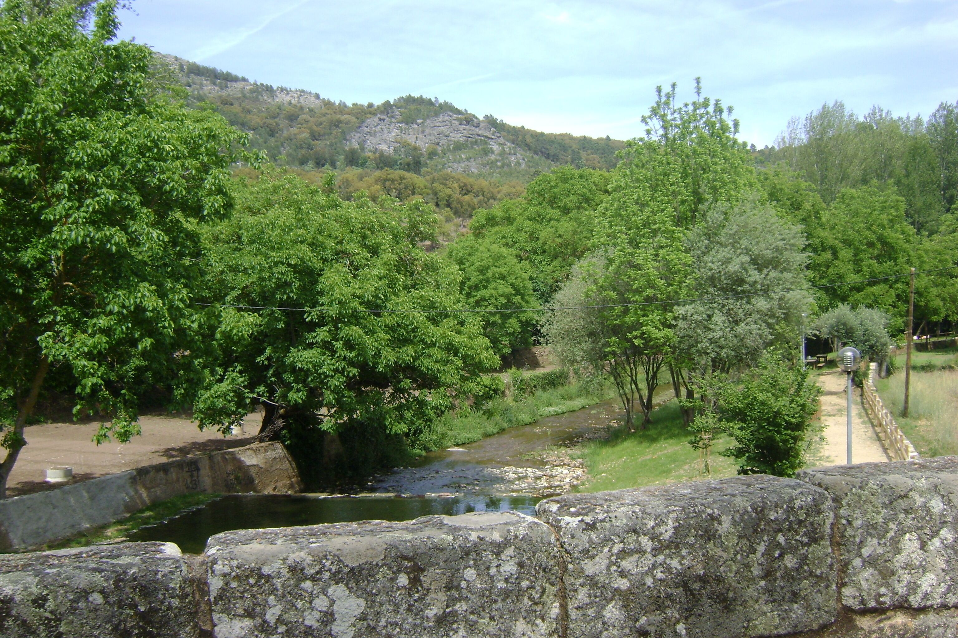 Eine Steinbrücke über einem Fluss, umgeben von üppigem Grün und einer hügeligen Landschaft.