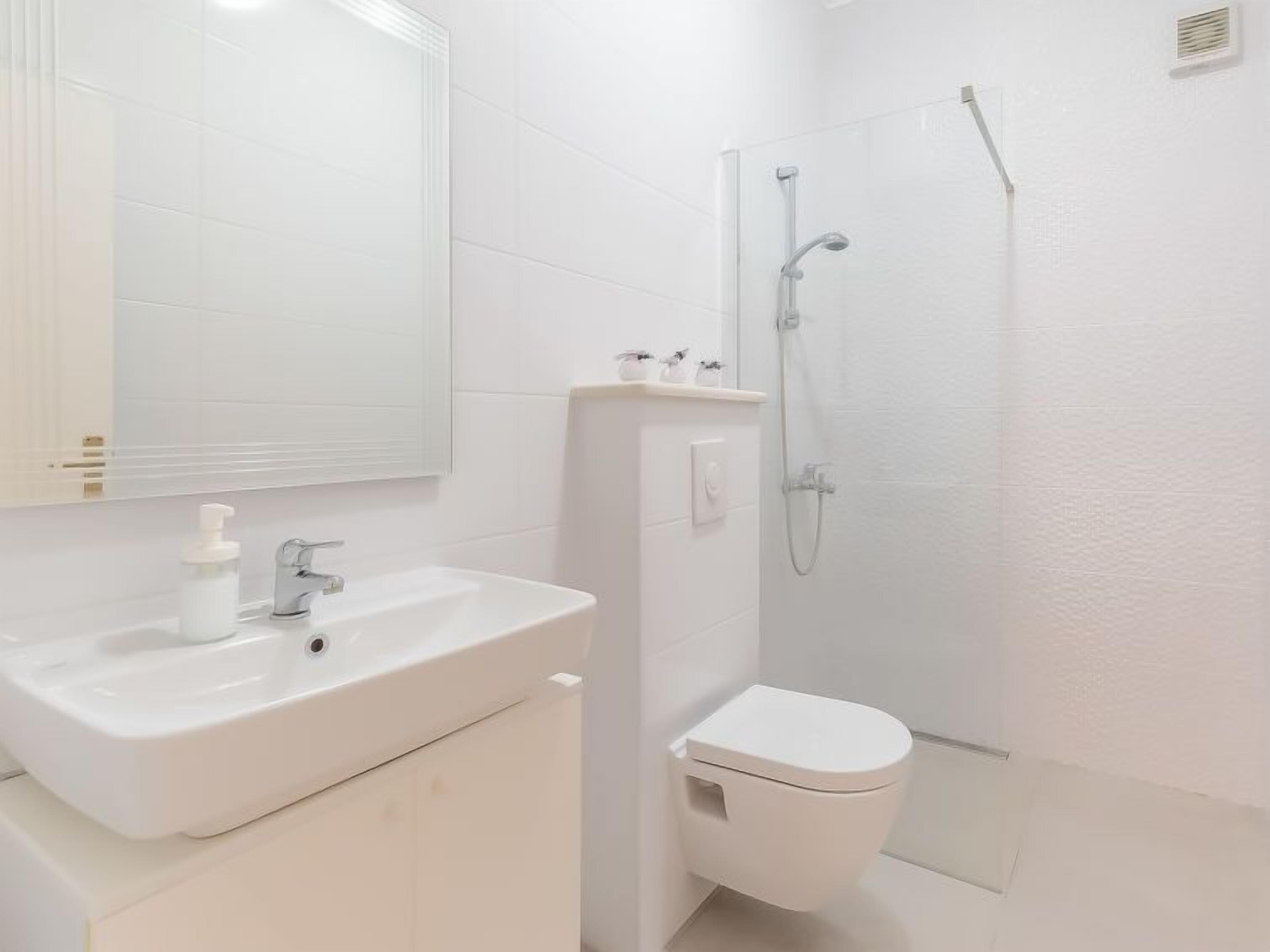 Un baño con lavamanos, inodoro y ducha blancos.
