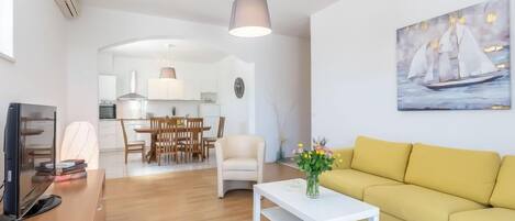 A modern living room with a yellow sofa, a white coffee table, and a painting of a sailboat.