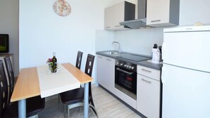 Une cuisine compacte avec des meubles blancs, un four encastré, un évier et une horloge au mur.