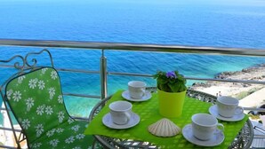 Une table dressée avec des tasses et des soucoupes, une plante en pot et un coquillage, le tout sur un balcon donnant sur la mer.