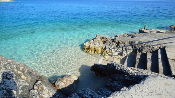 Un paysage côtier avec une eau bleue et limpide, un terrain rocheux et un escalier descendant vers la mer.