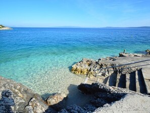 Un paysage côtier avec une eau bleue et limpide, un terrain rocheux et un escalier descendant vers la mer.