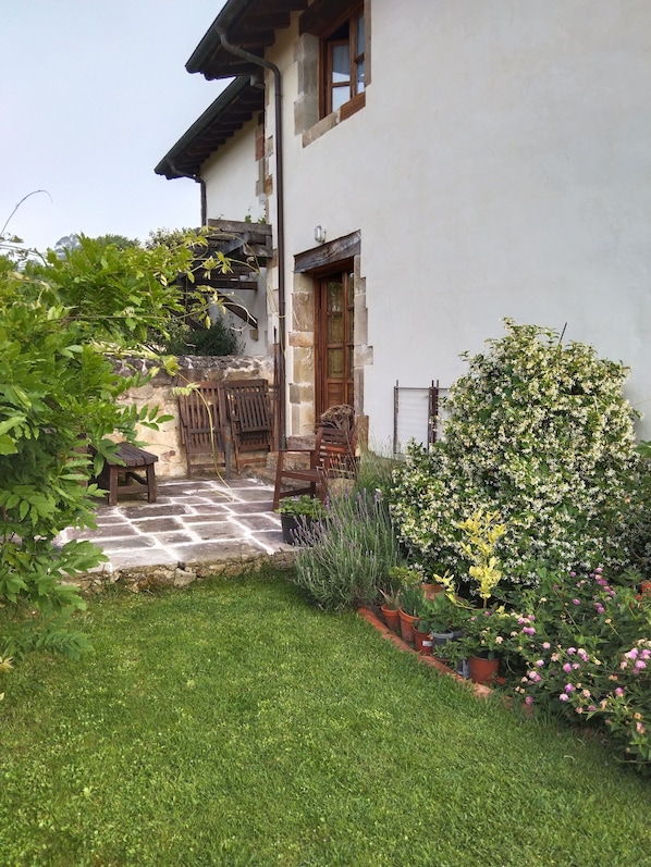 Et hus med en stentrappe, der fører op til en trædør, omgivet af en velplejet have med forskellige planter og blomster.