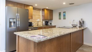 A modern kitchen with a granite countertop, stainless steel appliances, wooden cabinets, and a breakfast bar.