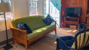 A cozy living room with a green sofa, a blue armchair, a television, and a wooden door. - Three bedroom cottage-Only .2 miles to Sea Street Beach (Dennis Port)