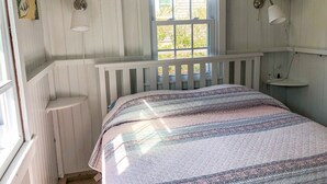 A bedroom with a bed, a window with a view, a wall-mounted fan, and a bedside lamp. - Three bedroom cottage-Only .2 miles to Sea Street Beach (Dennis Port)