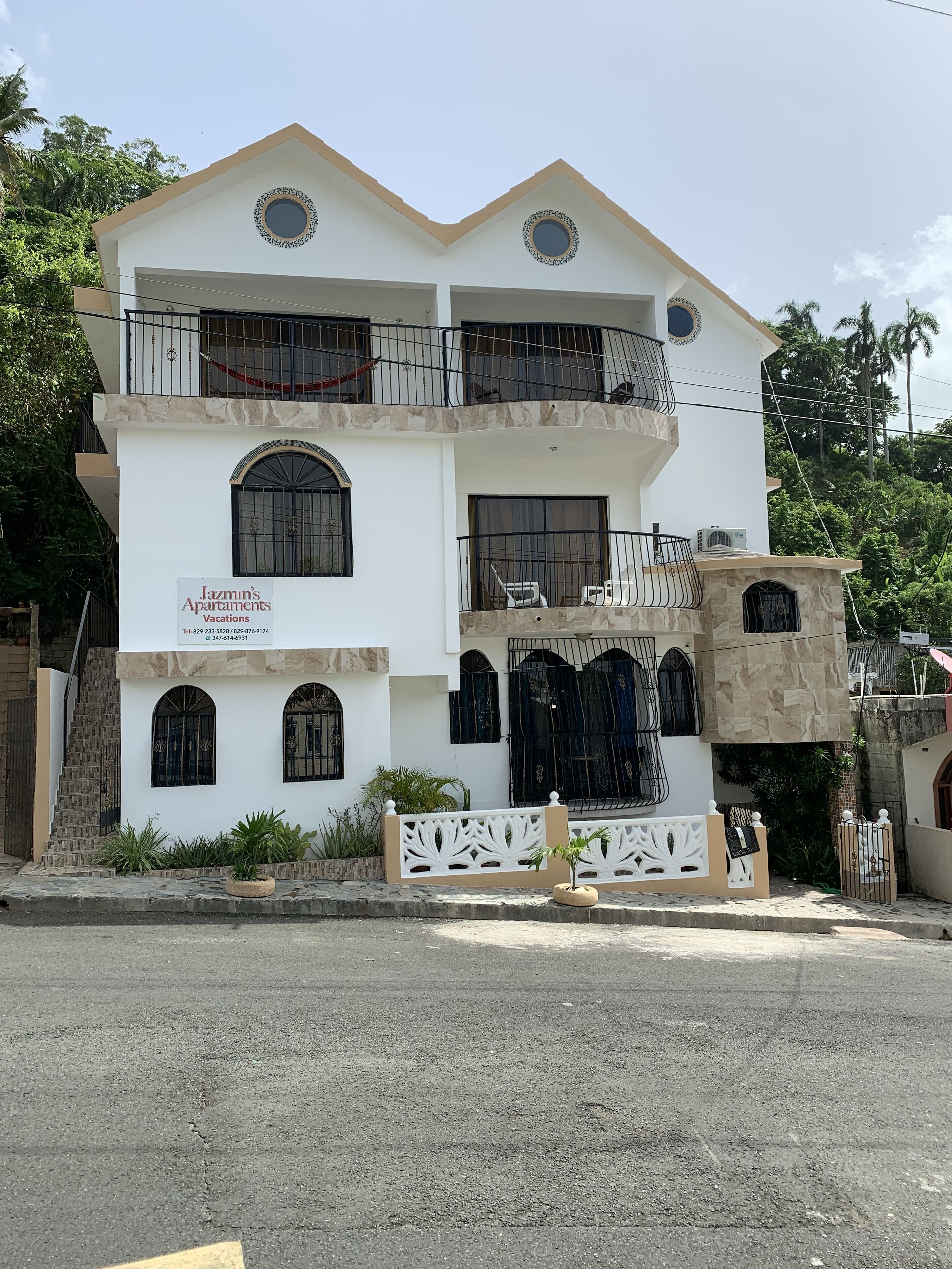 A multi-story building with balconies, a sign for Jazmin's Apartments Vacations, and a gated entrance.