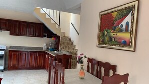 A dining area with a table set for four, wooden chairs, a vase with flowers, and a staircase leading to the upper floor. - Jazmin Apartments Vacations (Samaná)