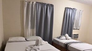 A hotel room with two beds, each with white bedding and pillows. There are grey curtains on the windows, and an air conditioning unit is visible on the wall. - Jazmin Apartments Vacations (Samaná)