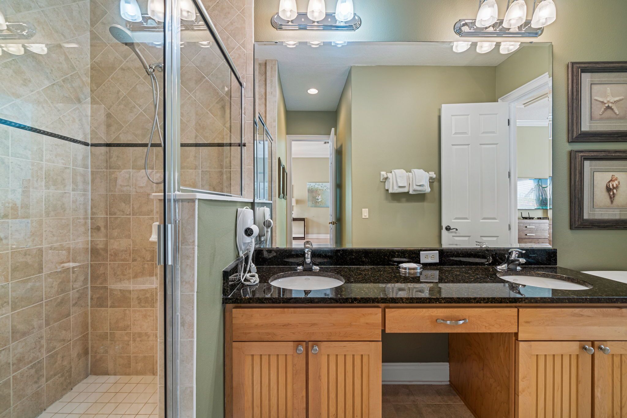 A bathroom with a glass shower enclosure, a vanity with two sinks, and a large mirror.