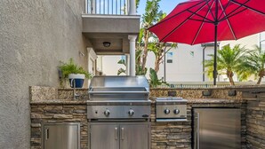 An outdoor kitchen with a built-in grill, a refrigerator, and stone walls.