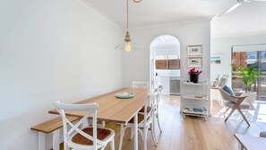 A modern dining area with a wooden table, white chairs, and a hanging light fixture. - Three bedroom unit at Little Beach (Nelson Bay)
