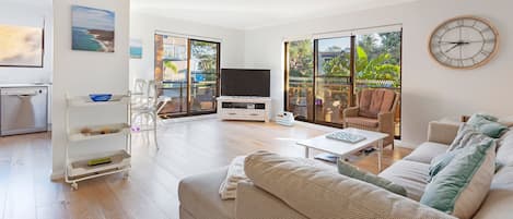 A modern living room with a sofa, coffee table, TV, and a large window with a view.