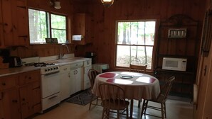 A wooden cabin kitchen with a dining table, chairs, a stove, a sink, and a microwave. - Little Beans Cottage on Great Pond, Belgrade ME (Rome)
