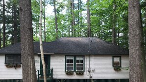 A cabin with a dark roof, white siding, and green trim. It has a front door, two windows, and a small porch with a bench. - Little Beans Cottage on Great Pond, Belgrade ME (Rome)