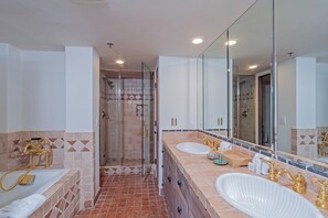 A bathroom with a glass shower enclosure, two sinks with gold faucets, and a large mirror.