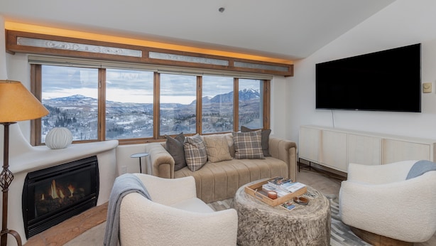 Una sala de estar moderna con chimenea, un ventanal con vistas a la montaña, un televisor de pantalla plana en la pared y una zona de estar acogedora.
