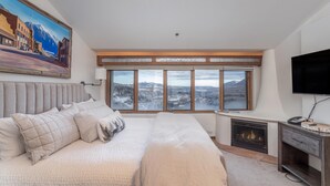 Un dormitorio con una cama grande, una chimenea, un televisor y vistas panorámicas desde las ventanas.