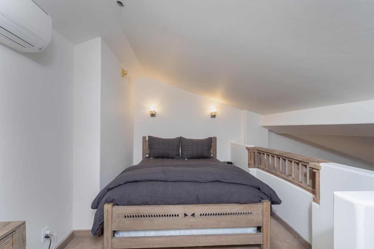 Un dormitorio con cama, lámparas de noche, cabecero de madera y pared blanca.