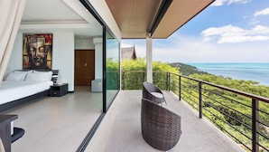 A modern bedroom with a large bed, a nightstand, and a painting. There is a balcony with a wicker chair and a view of the ocean. - Ban Nai Fan: 3 Bed Pool Villa w/ Magnificent Sea View (Ko Samui)