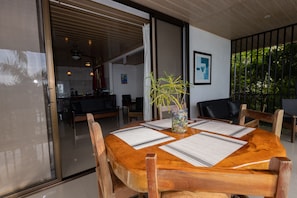 A wooden dining table with placemats, surrounded by chairs, in a modern kitchen area with sliding glass doors leading to a balcony. - Panoramic Villa - vacational home rental (Quepos)