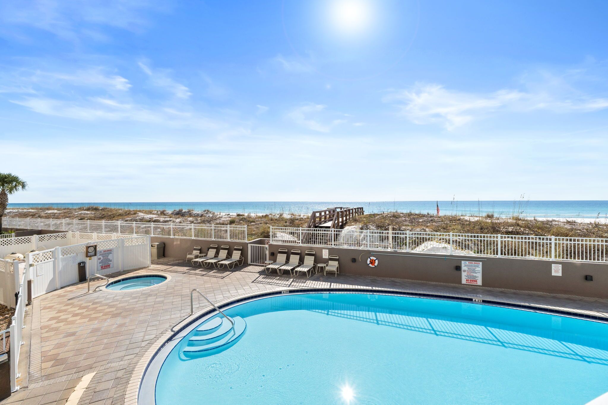 Un espace piscine avec vue sur la plage, des chaises longues et un panneau indiquant la présence d’un sauveteur.