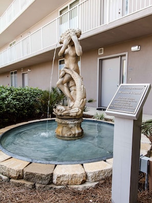 Stunning stone fountain features a statue of a woman holding a fish, surrounded by a low wall in a serene outdoor setting.