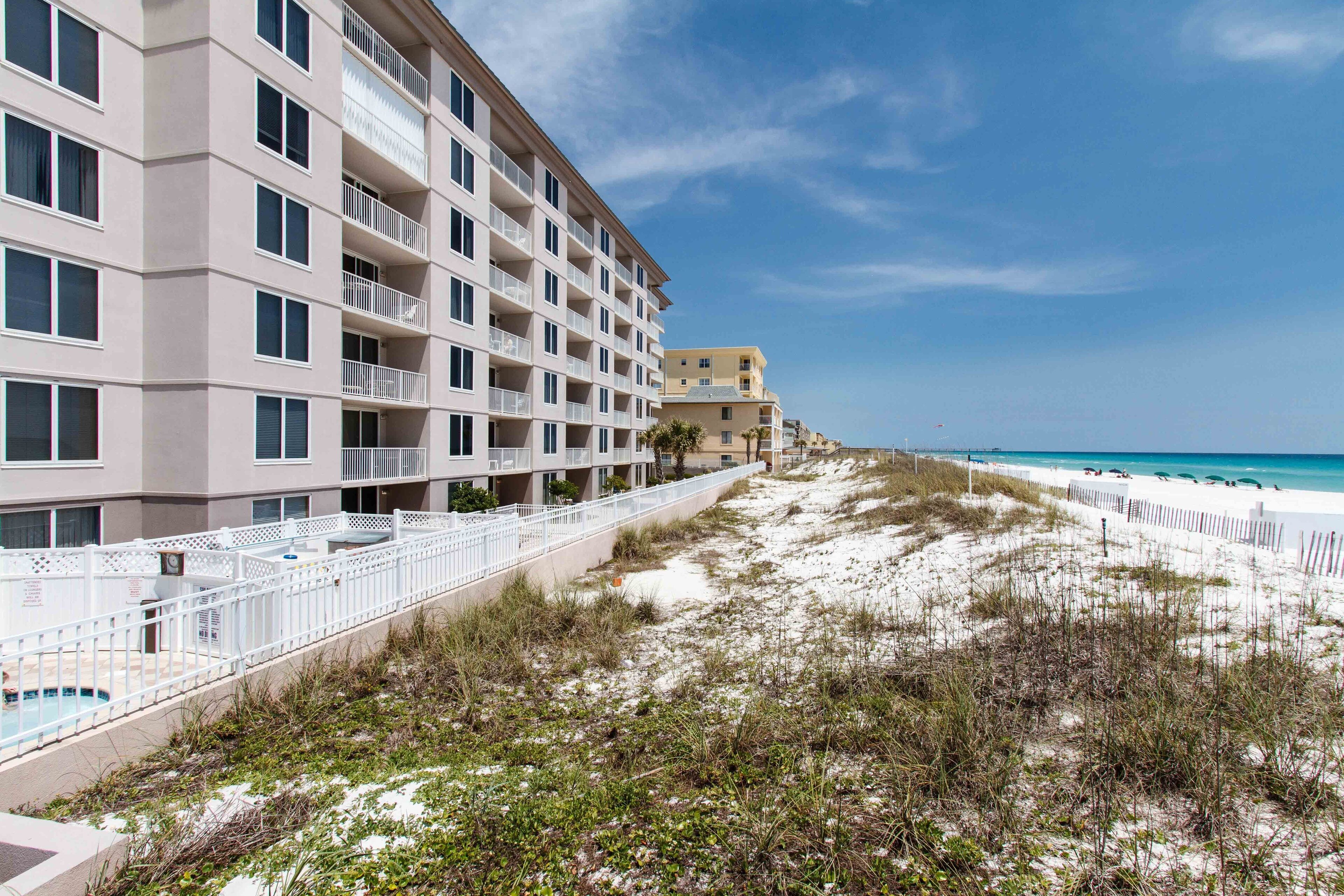 A beachfront hotel with multiple balconies, a pool, and a sandy beach area.