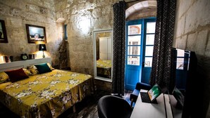 Een kamer met een bed, een bureau, een stoel, een spiegel, een raam met gordijnen en een wandklok.