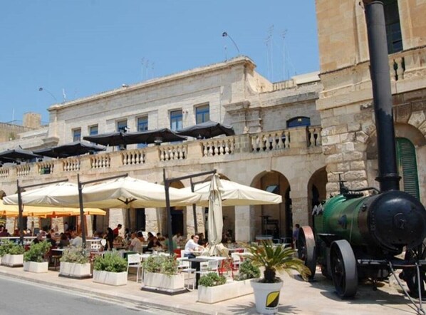 An outdoor cafe with stone buildings, outdoor seating, and a steam engine. - Cosy Townhouse in Historic centre (Il-Birgu)