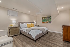 Ein Schlafzimmer mit einem großen Bett, zwei Nachttischen, einem Beistelltisch, einer Holzkassette und einem farbenfrohen Bild an der Wand.