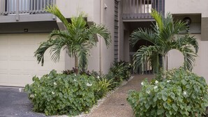 A residential building with a garage door, a gravel pathway, and several potted plants including palm trees and a flowering shrub. - Steps to#1 rated Beach in USA Spacious2+2Condo,pool,garageTranquil Setting (Siesta Key)