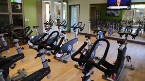 Un gimnasio con varias bicicletas estáticas, una pantalla de televisión y un espejo que refleja las bicicletas.