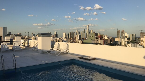 A rooftop pool with lounge chairs and a city skyline view.