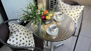 A glass-top table with a vase of flowers, a fruit bowl, and two cups on a tiled floor.