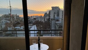 A balcony with a table and chairs, overlooking a cityscape during sunset.
