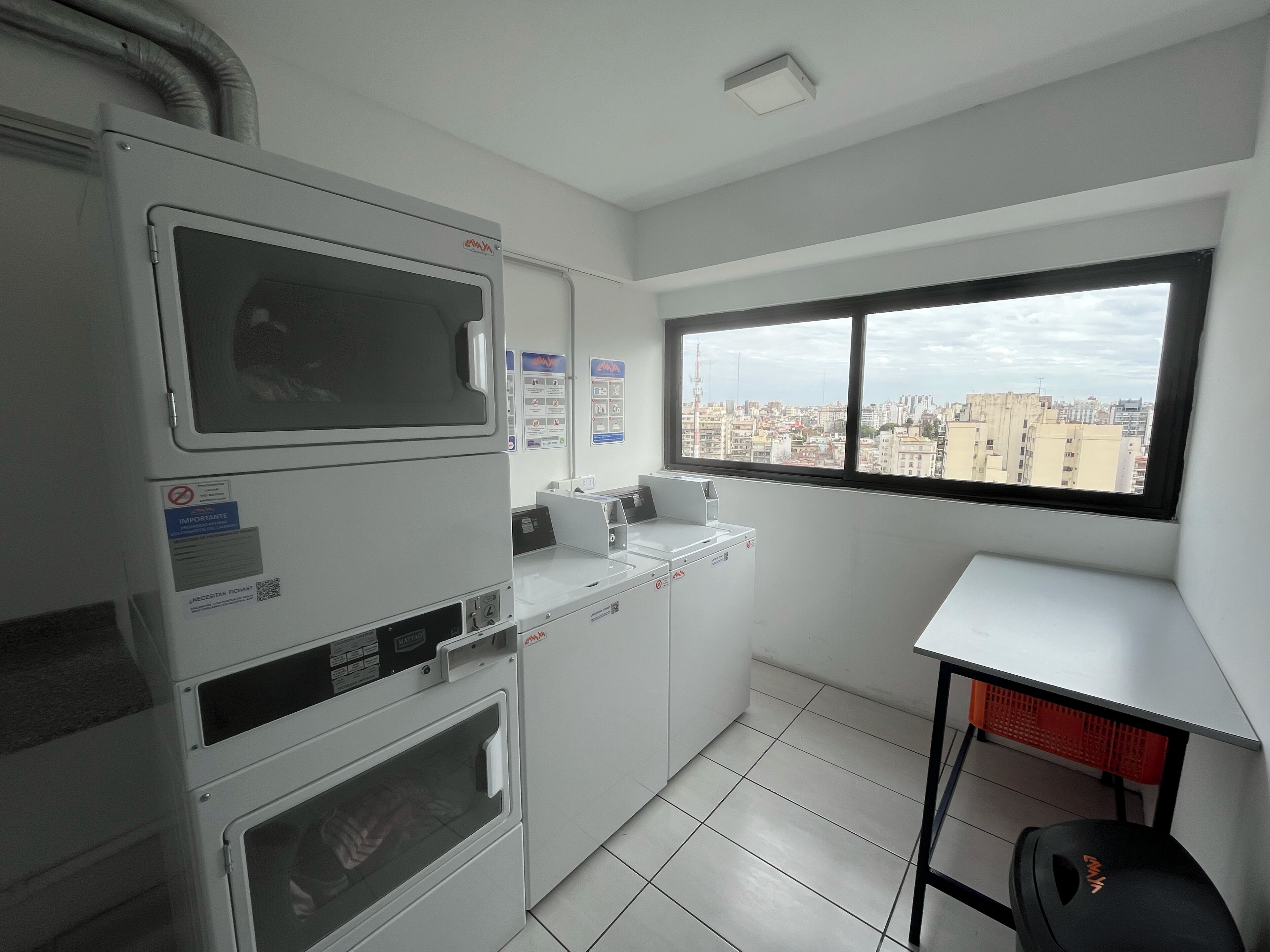 A compact kitchen with a microwave, oven, and sink, a small table, and a window with a city view.